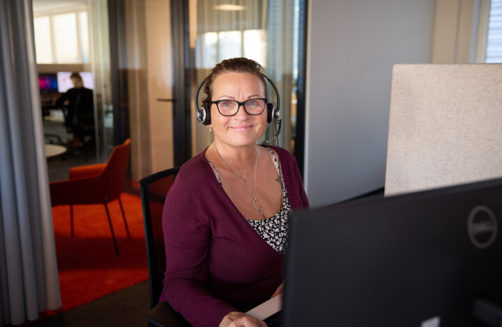 L&auml;chelnde Kundenbetreuerin mit Headset vor einem Monitor.